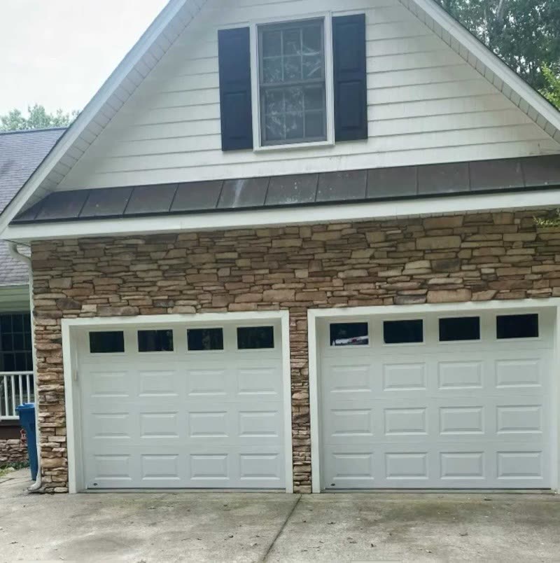 Two new white garage doors with windows on a stone-front garage